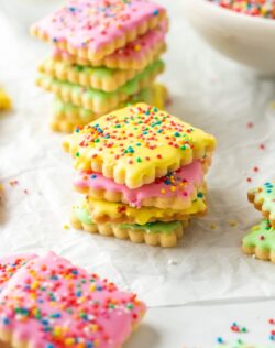 different coloured iced cookies covered in sprinkles on a sheet of baking paper