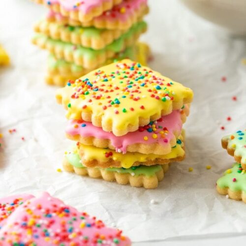 different coloured iced cookies covered in sprinkles on a sheet of baking paper