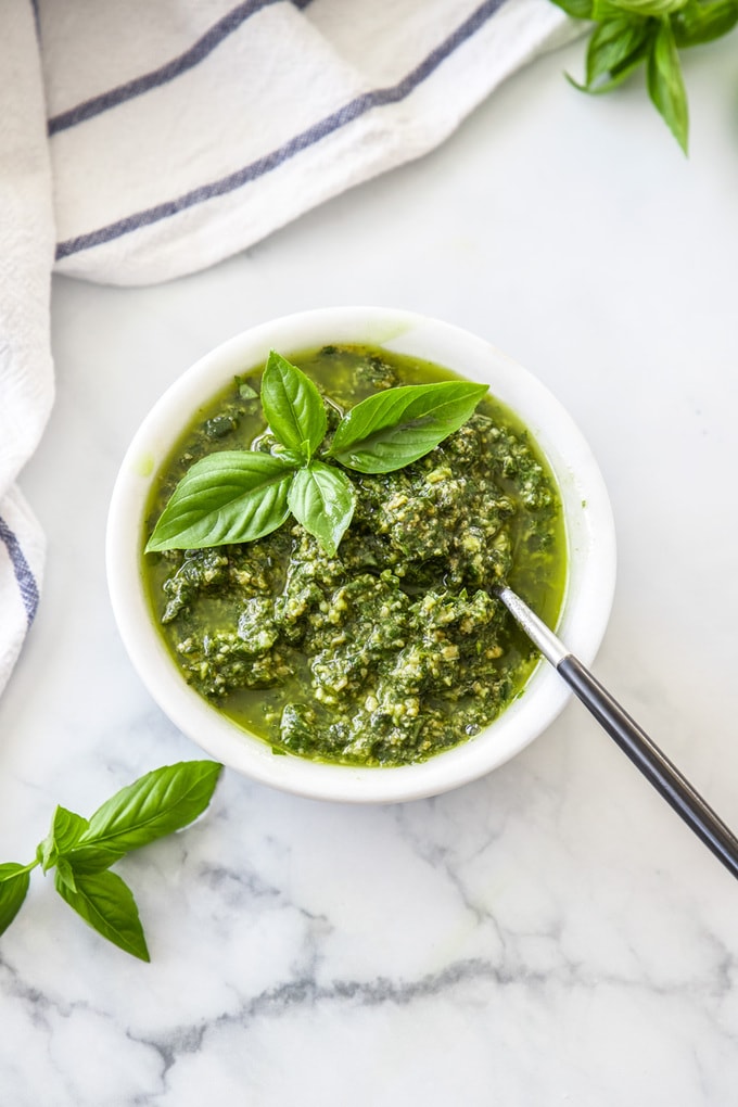 A white bowl filled with pesto on a marble benchtop.