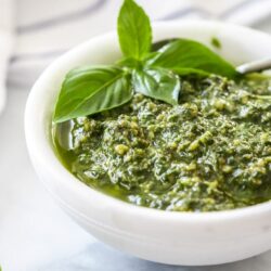 A white bowl filled with pesto on a marble benchtop.
