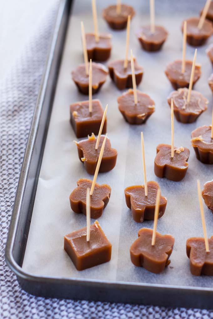 Butterscotch candies on a baking tray with toothpicks stuck in them.