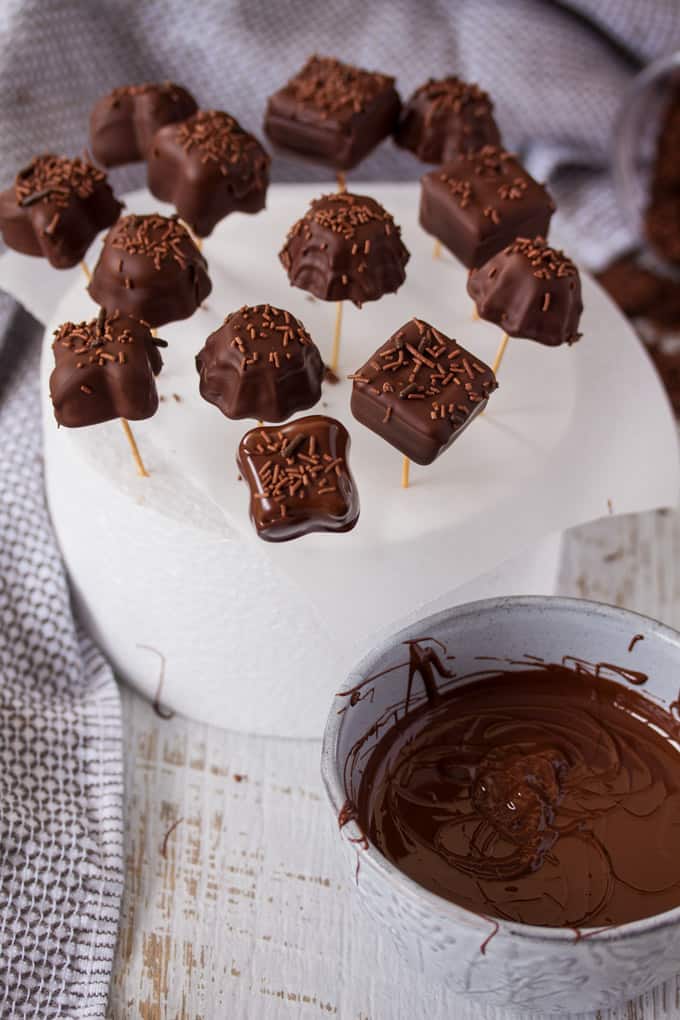 Chocolate candies on toothpicks setting, with a bowl of melted chocolate in front.