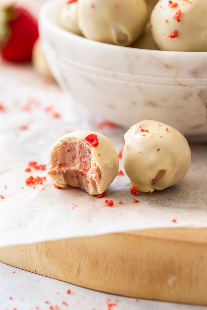 A closeup of 2 white chocolate truffles with pink insides. One has a bite taken out of it.