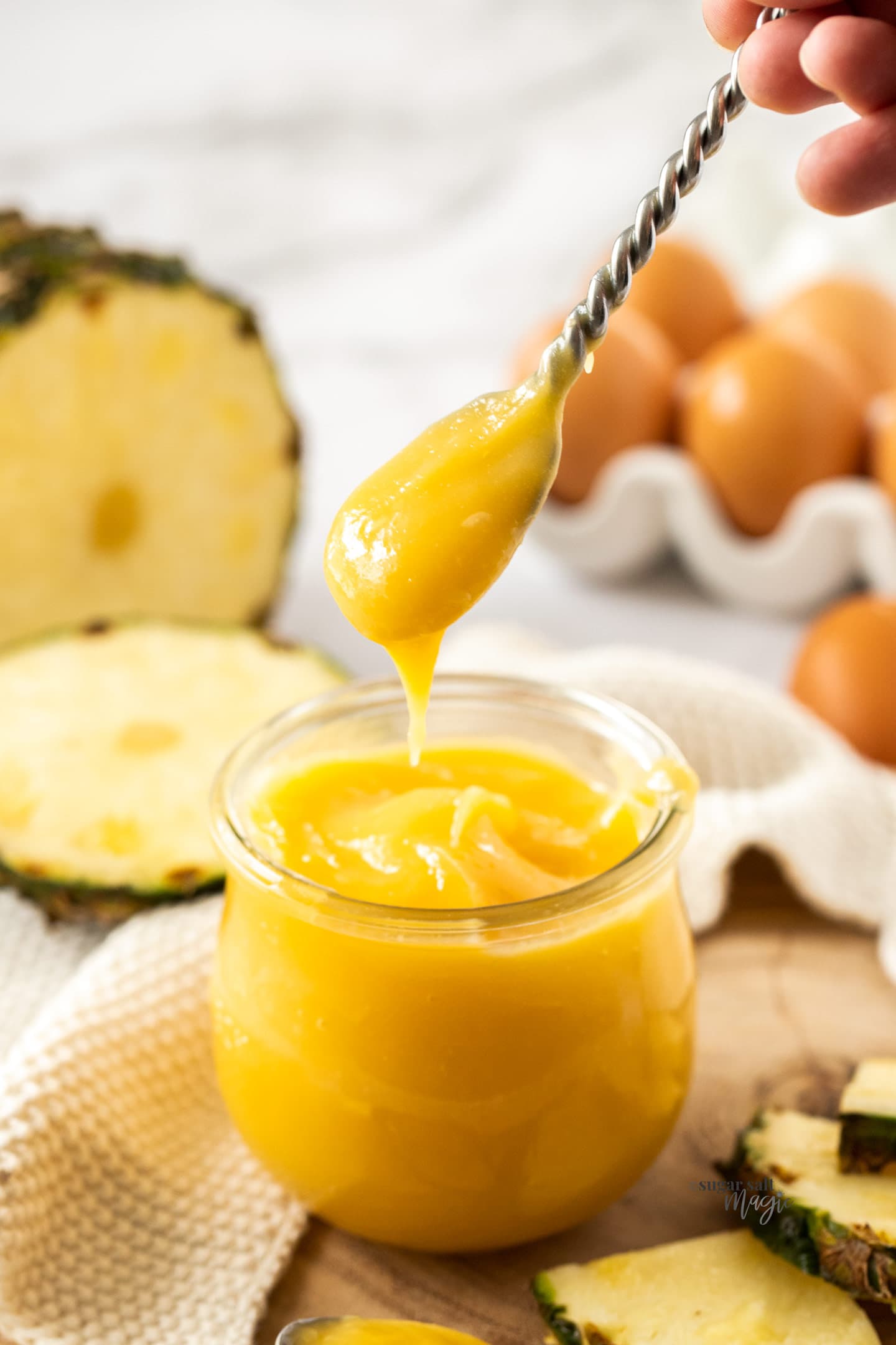 A spoon taking pineapple curd from a glass jar