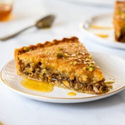 A slice of baklava tart on a white plate with syrup drizzling down the side