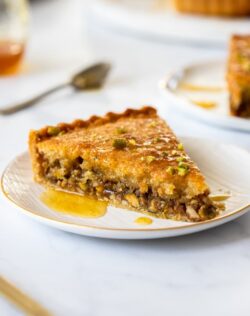 A slice of baklava tart on a white plate with syrup drizzling down the side