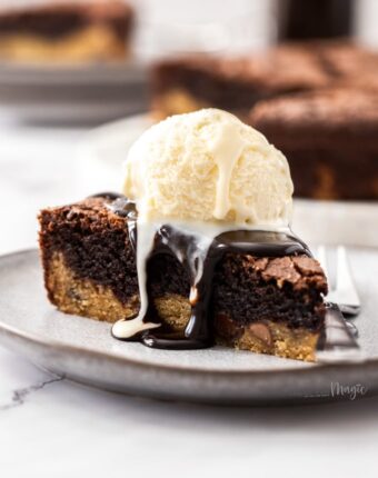 A slice of brookie pie on a grey plate with chocolate sauce oozing down the sides and a scoop of ice cream on top