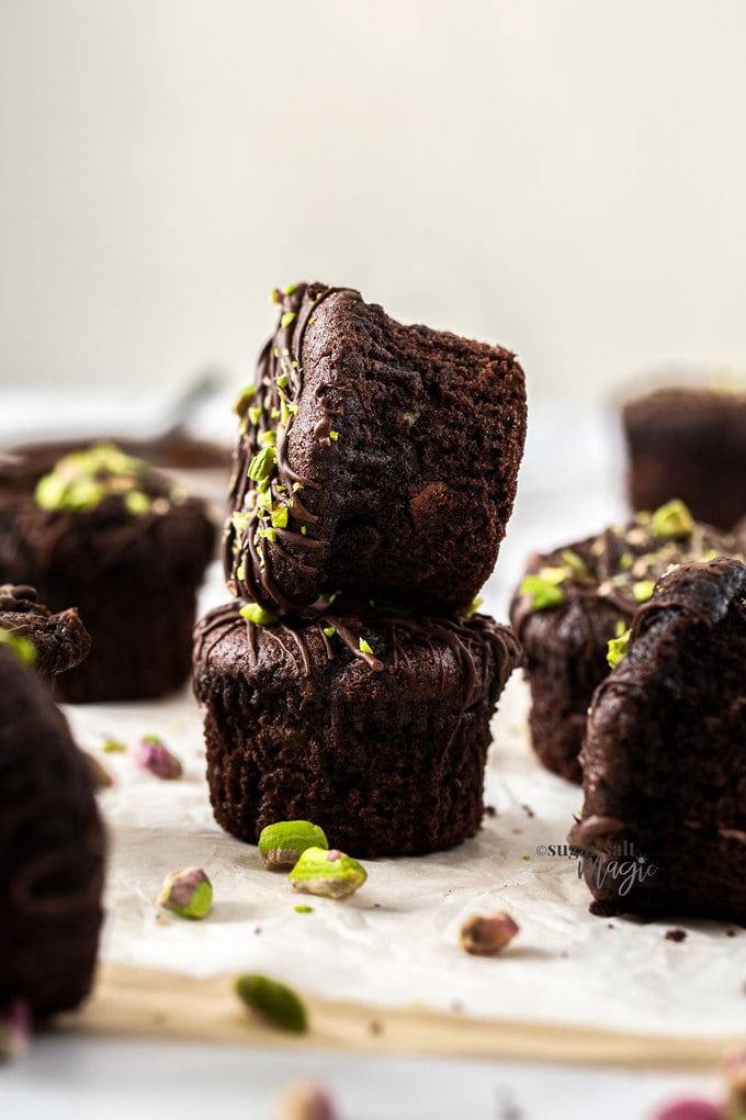 Two chocolate muffins stacked, surrounded by more muffins and pistachios
