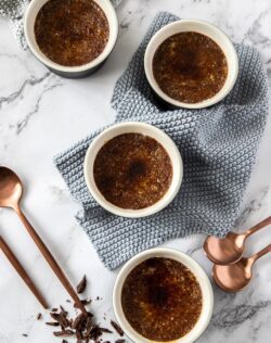4 chocolate creme brulees on a marble table with bronze coloured spoons next to them