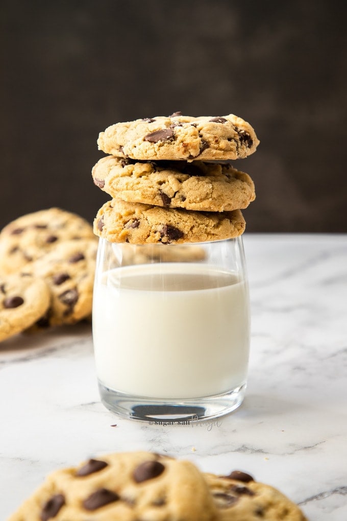 A stack of 3 chocolate chip cookies on top of a glass of milk