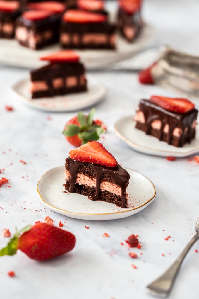 Chocolate petit fours sitting on mini white plates with strawberries surrounding them