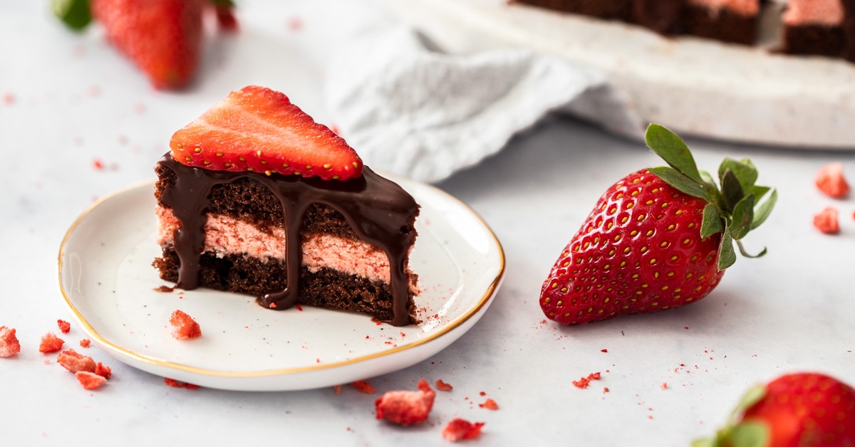 A closeup of a chocolate petit four sitting next to a strawberry