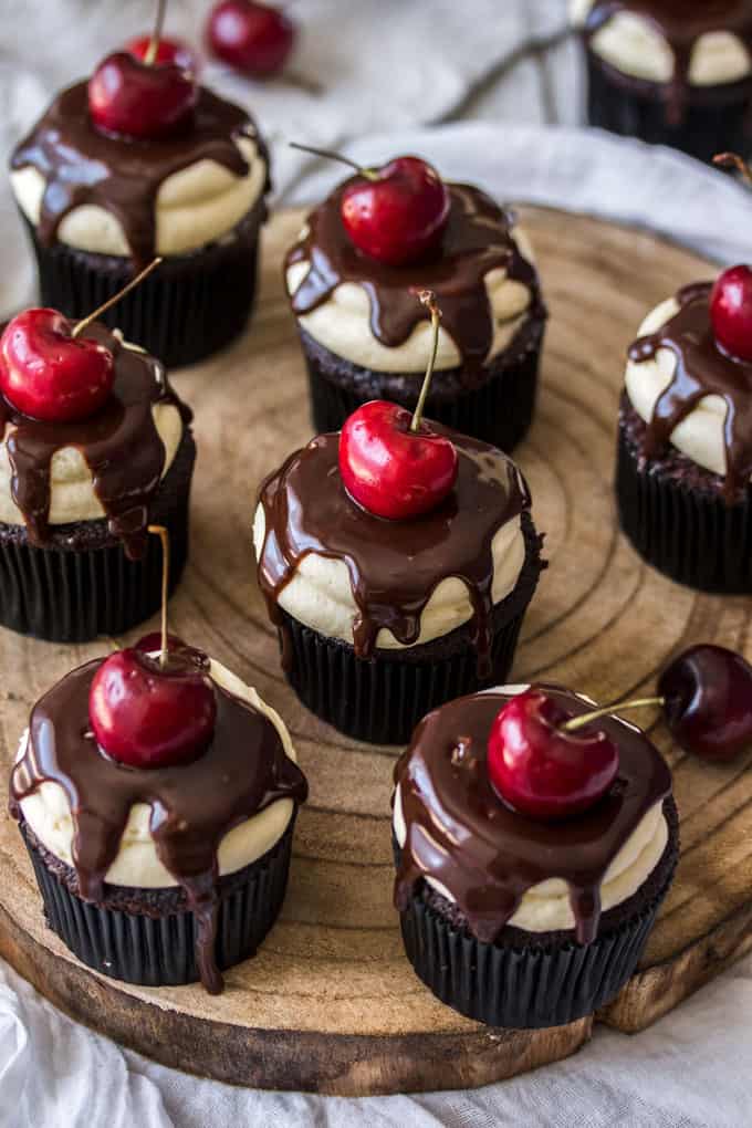 Cupcakes topped with chocolate and a fresh cherry on a wooden board. 