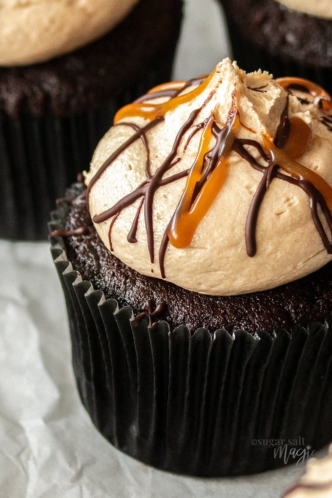 Extreme closeup of a chocolate cupcake in a black wrapper topped with caramel buttercream and streaks of caramel sauce.