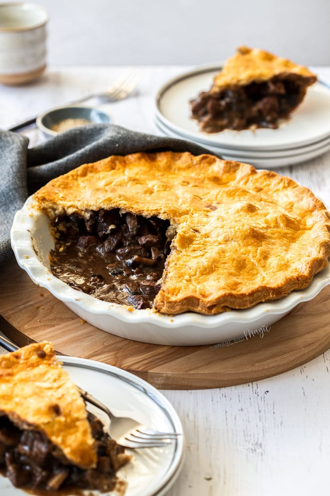 Beef pie in a white pie dish showing the inside. It sits on a wooden board.