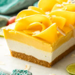 A dessert with 3 layers in a loaf shape on a marble cake plate. Topped with slices of mango.