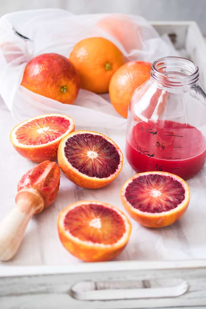 Blood oranges and a jar of blood orange juice on a white tray.