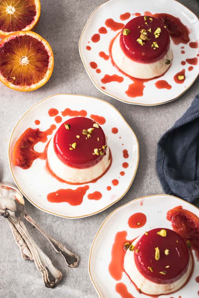 3 Panna Cotta with blood orange jelly on white plates.