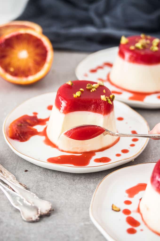 A spoon taking a scoop of panna cotta with blood orange jelly on top.