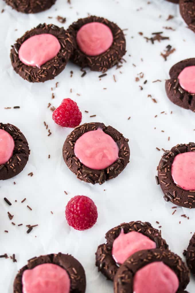 Chocolate Raspberry Thumbprint Cookies, fresh raspberries and chocolate sprinkles on a white surface.