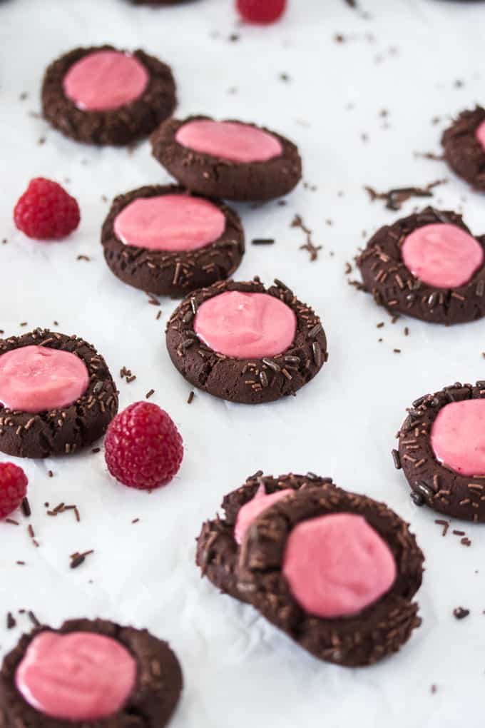 Chocolate Raspberry Thumbprint Cookies scattered on a white surface in random positions.