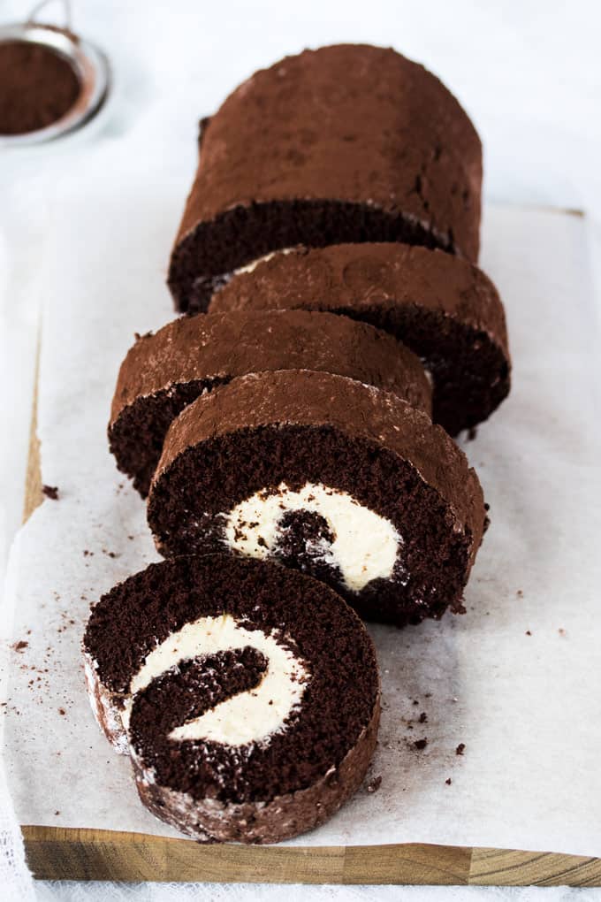 A chocolate roll cake cut into slices on a sheet of baking paper.