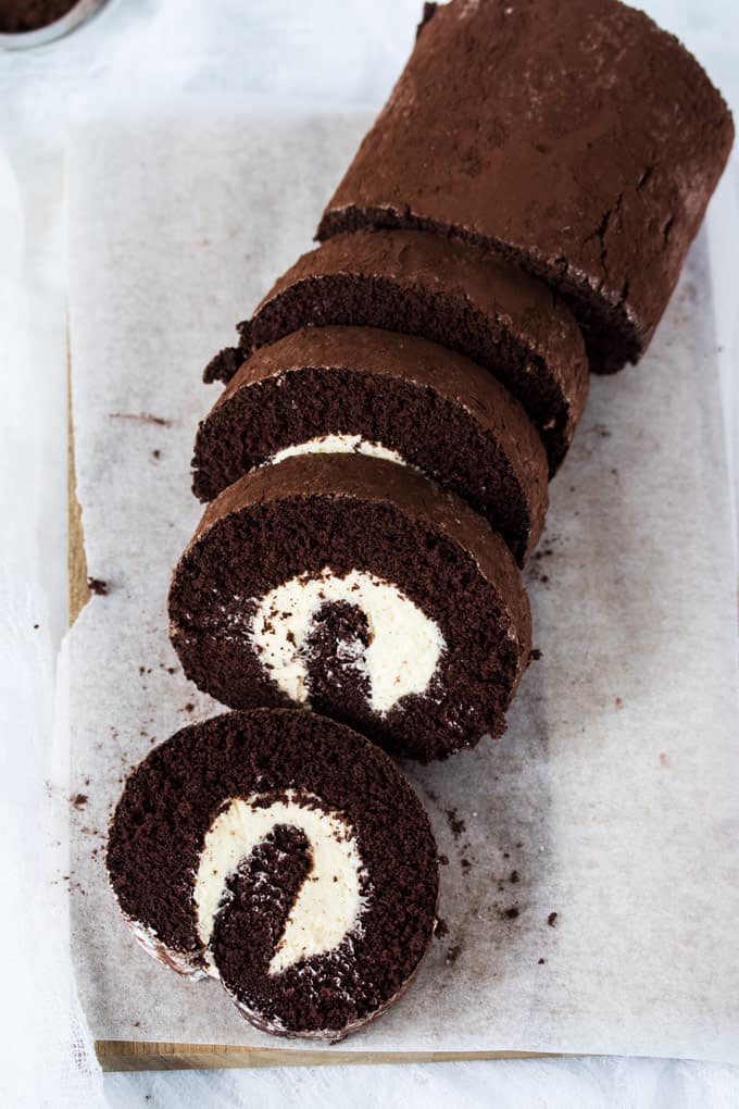 A chocolate roll cake dusted with cocoa on a wooden board.