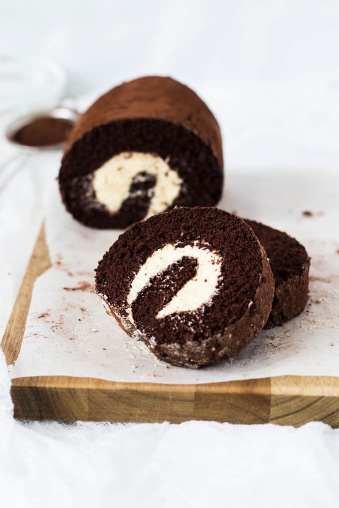 Slices of chocolate roll cake stacked againsted one another on a wooden board.