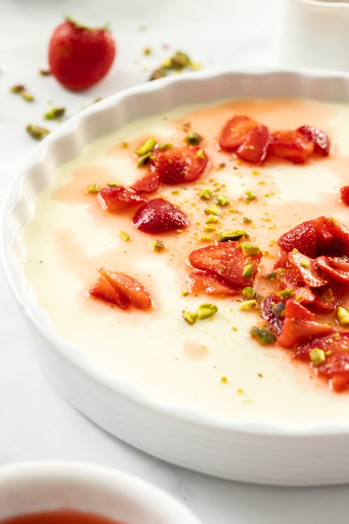 A large white dish filled with panna cotta. Some macerated strawberries sit on top and in front.