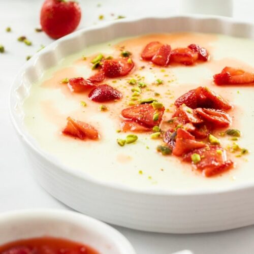 A large white dish filled with panna cotta. Some macerated strawberries sit on top and in front.