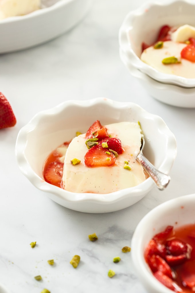 A white dish filled with panna cotta with strawberries on top