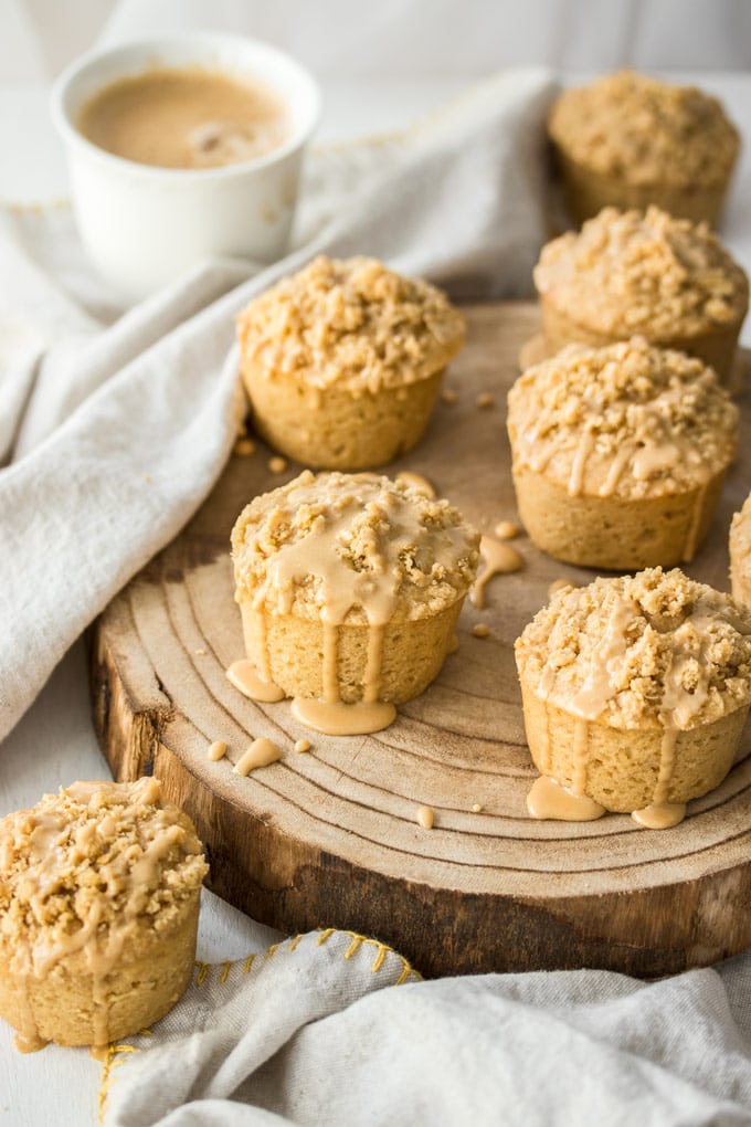 7 Coffee Cake muffins on a board with a cup of coffee in the background.