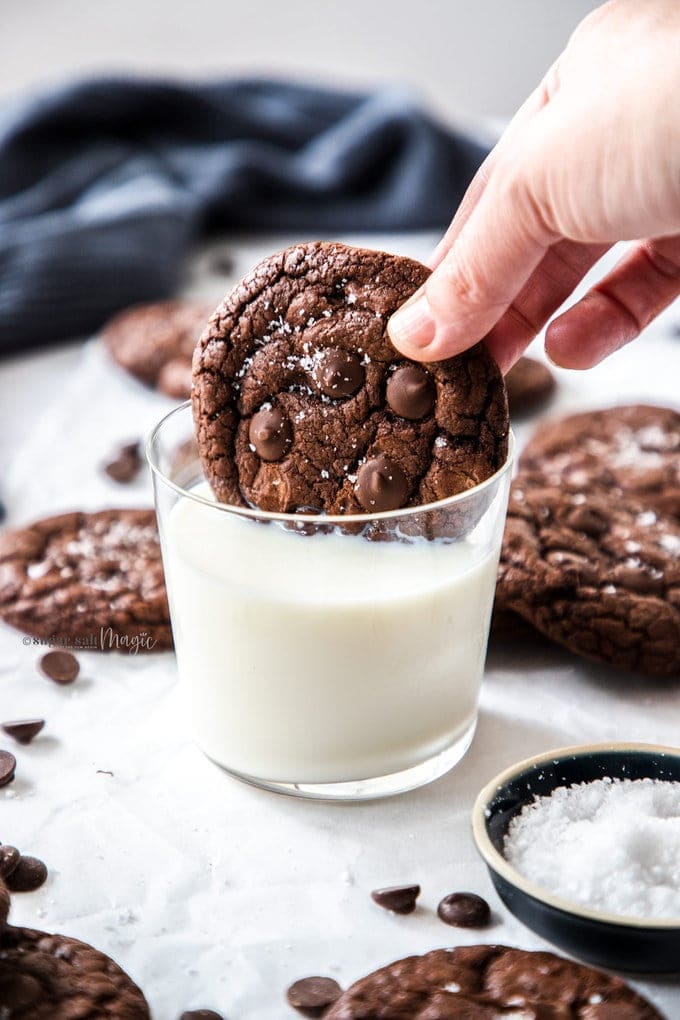 A chocolate cookie being dunked into a glass of milk.
