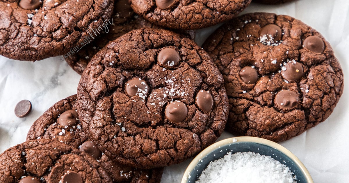A batch of chocolate cookies piled next to a small dish of salt flakes