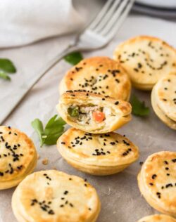 A batch of miniature chicken pot pies with one broken open showing the filling.