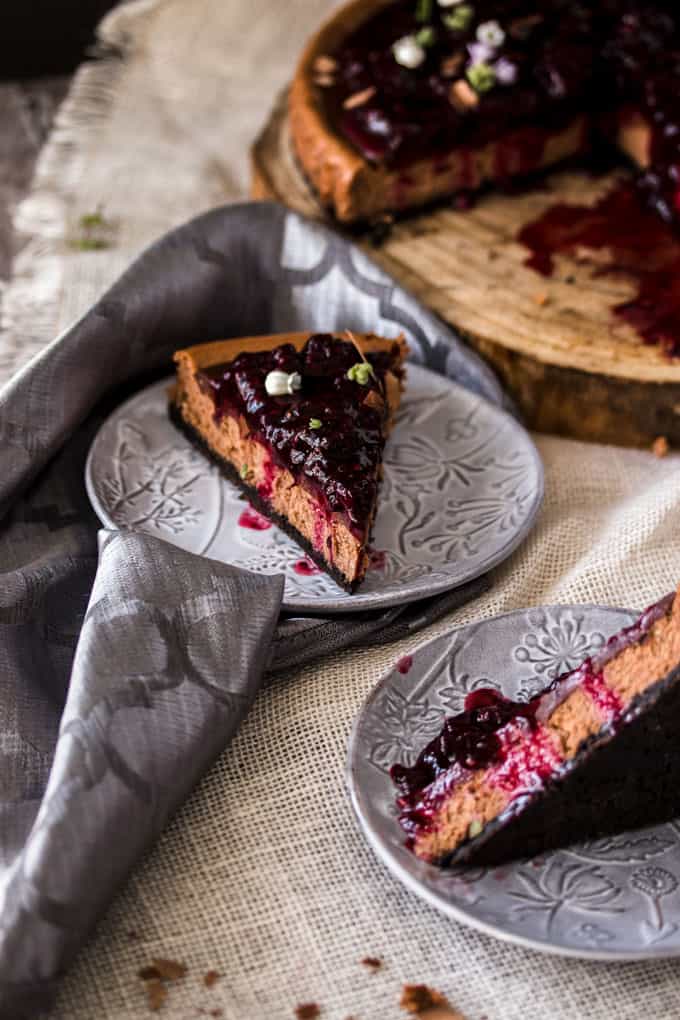 A slice of Baked Chocolate Cheesecake with Blackberry Compote on a gray plate, another slice laying on its side on another plate.