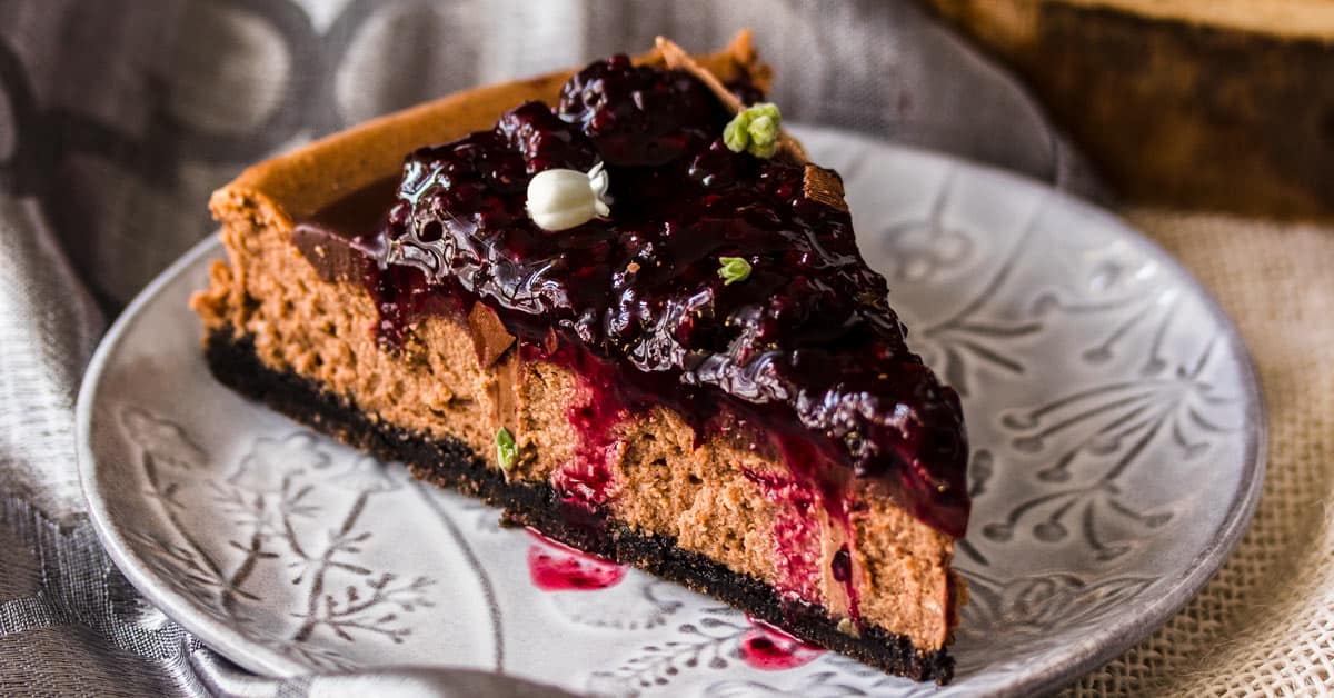A slice of Baked Chocolate Cheesecake with Blackberry Compote on a gray patterned plate.