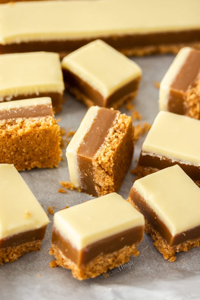 squares of caramel slice covered in white chocolate on a sheet of baking paper