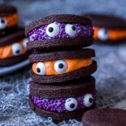 A stack of 3 chocolate cookies with candy eyes stuck to them.