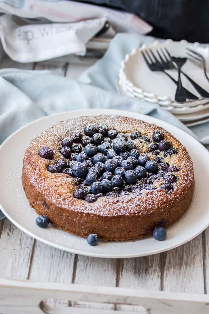A blueberry cake on a white plate sitting on a wooden tray.