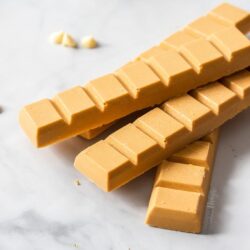 A stack of blocks of caramelised white chocolate with white chocolate chips scattered around them, on a marble surface.