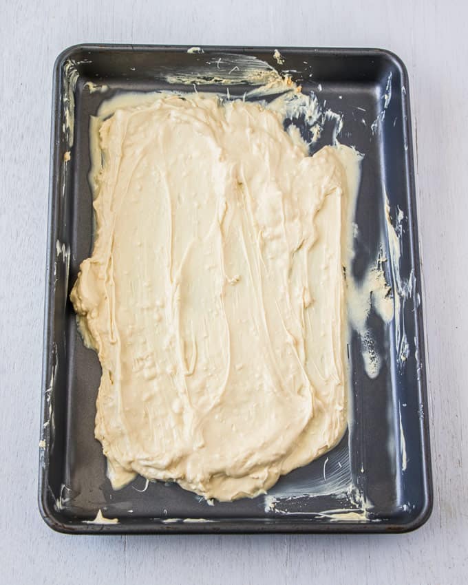 A baking tin covered in melted white chocolate that is being caramelised.
