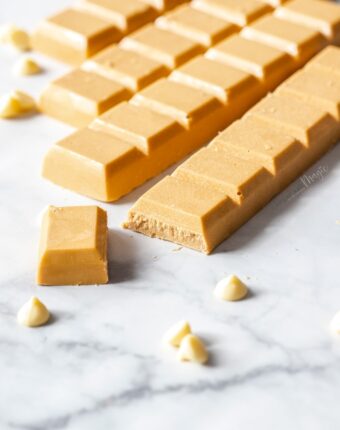 Bars of caramelised white chocolate on a marble surface, surrounded by white chocolate chips