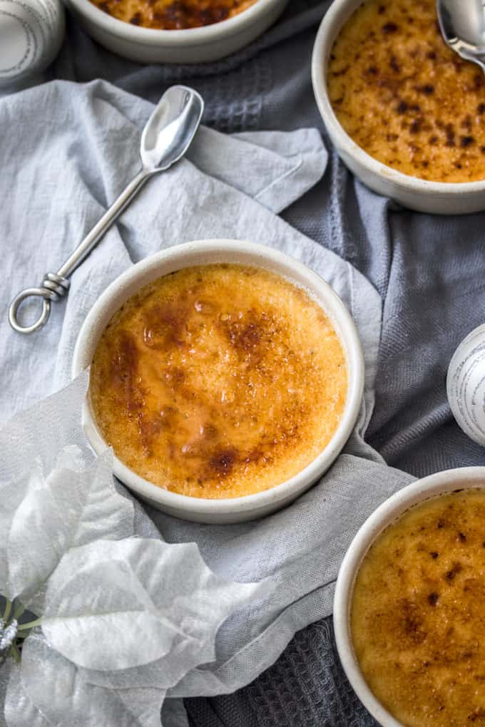 An Eggnog Creme Brulee in a white pot on top of a white towel next to a spoon.