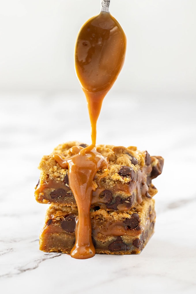 Caramel being poured from a spoon onto 2 cookie bars below it