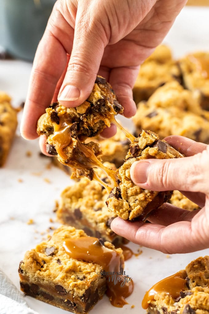 A hand pulling apart a cookie bar showing the caramel inside