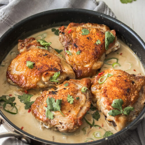 A black skillet filled with chicken thigh cutlets in a creamy sauce.