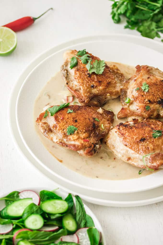 4 pieces of chicken thighs in creamy sauce on a white plate.