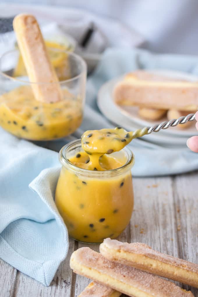 A spoon filled with passionfruit curd coming up from a jar.