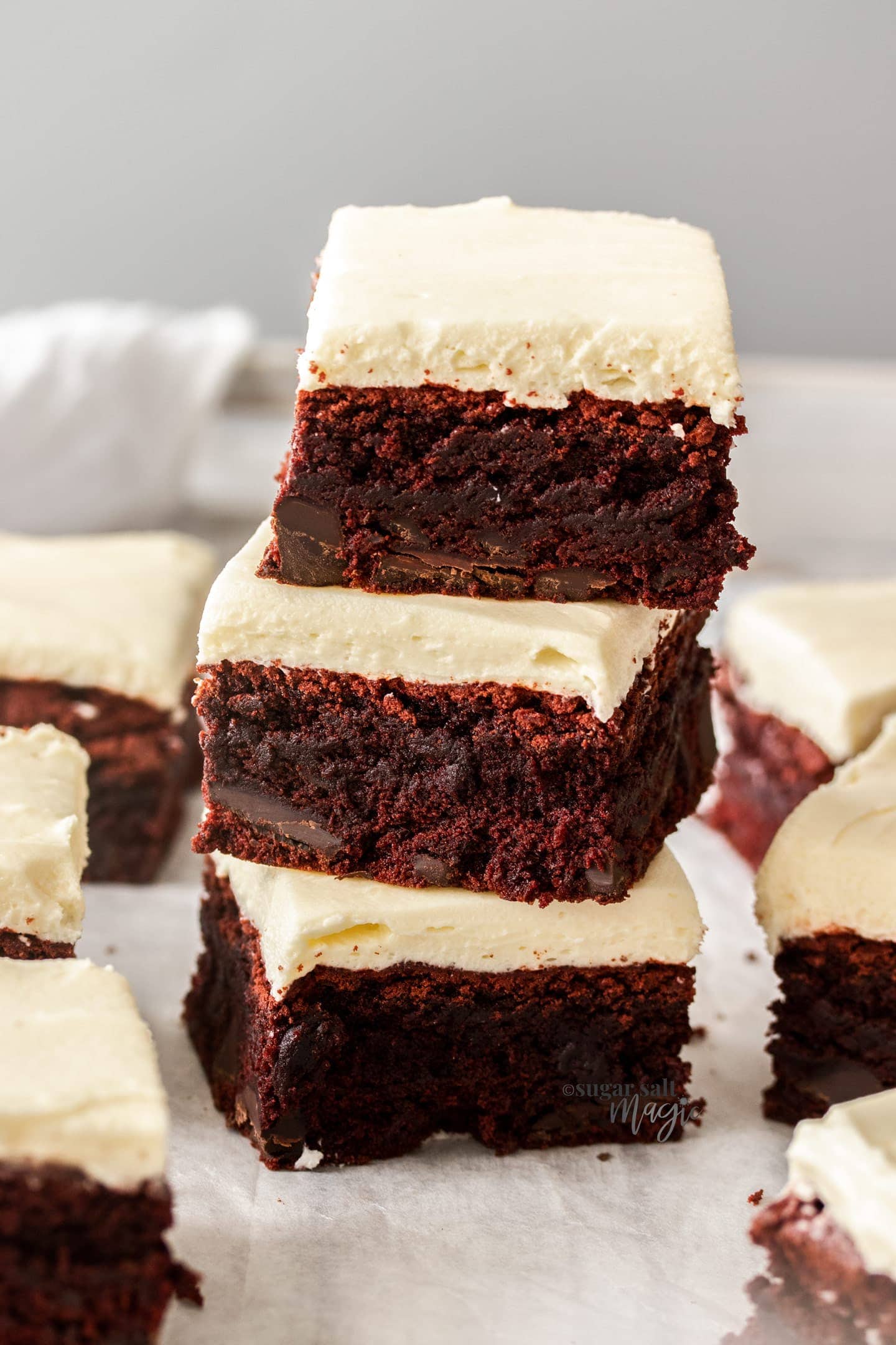 A stack of 3 red velvet brownies with more around it.